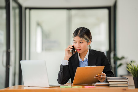 Young accountant working with smartphone and laptop with financial graph documents on tableの写真素材