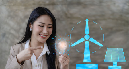 Young Asian businesswoman holding a light bulb presenting energy saving with wind turbine and solar cells icon.の写真素材