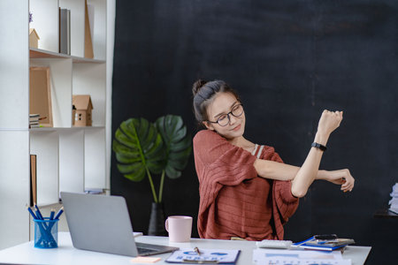 Asian woman stretching arms to relax while working on laptop and concept finance graph office syndromeの写真素材