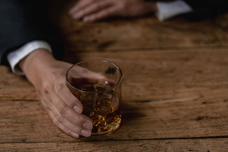 Close-up of serious businessman holding whiskey glass shows concept of executive privilege. Soft focus. Close-up view of two men in formal wear whiskey clashing glasses.の写真素材