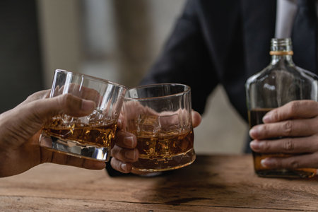 Close-up of serious businessman holding whiskey glass shows concept of executive privilege. Soft focus. Close-up view of two men in formal wear whiskey clashing glasses.の写真素材