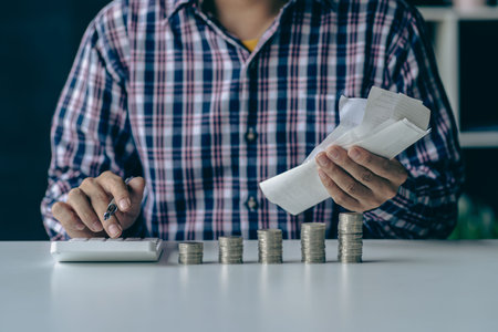 Stacks of coins and calculators placed on a wooden floor and growing money saving ideas.
Asian man writing monthly expense summary, coin bill piled on white table. Concept of saviの写真素材
