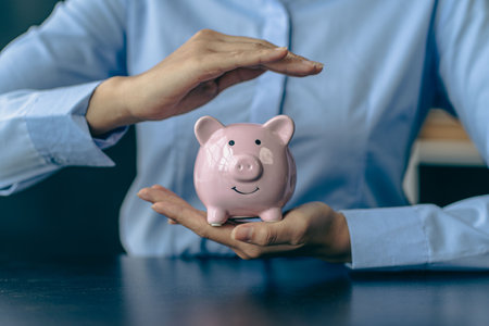 Woman's hand protects a piggy bank, saving money with a pile of coins. Step into a Successful Growing Business Saving Ideasの写真素材