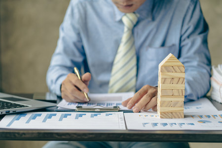 Business Crisis Concept : Hands pointing to financial business graph to analyze market problems. Statistical report graph financial documents with wooden block tower next to it.の写真素材