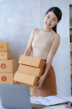 Young Asian woman working at home online selling on a box and laptop for SME business. Parcel delivery concept.の写真素材