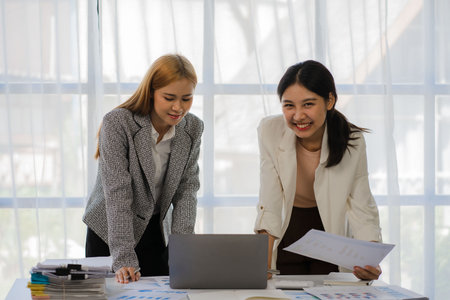 Finance concept and collaboration Two young female accountants in casual clothes work on laptops and financial graph documents and discuss company investment results and annual proの写真素材