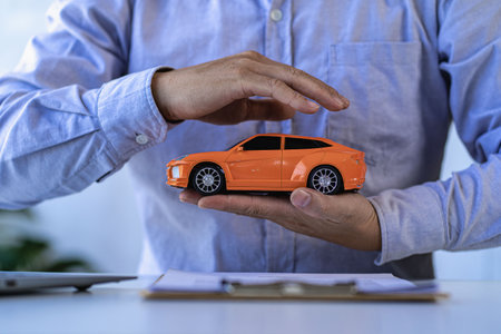 Car insurance. Small orange car. Hands. Businessman protects toy car.