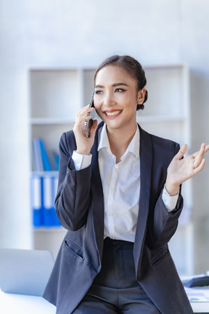 Asian businesswoman using smartphone and laptop to contact customers, calculate with calculator on desk, reading financial graphs, planning, analyzing, calculating market data in cの写真素材