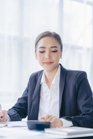 Economic concept Asian female accountant or banker calculating financial accounts. Young Asian businesswoman at work. Documents, taxes, analysis reports, savings and finances.の写真素材