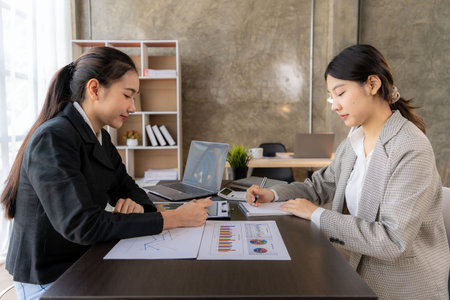 Two young asian accountants working on laptop computer and finance at workplace. Freelance business. Online marketing. ecommerce marketing ideasの写真素材