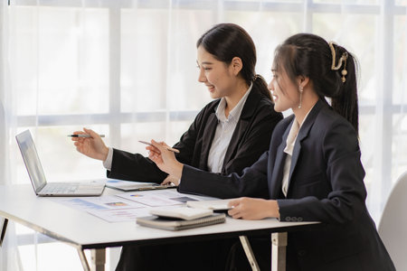 Two young asian accountants working on laptop computer and finance at workplace. Freelance business. Online marketing. ecommerce marketing ideasの写真素材