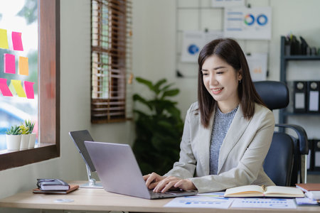 Asian businesswoman working on financial paperwork using laptop online tax, loan, bank debt for mathematical finance on desk, accounting, statistics and analytical research conceptの写真素材