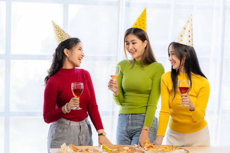 A party of three beautiful Asian girls are celebrating. Woman eating pizza on table with snacks and drink, happy on Christmas Eveの写真素材