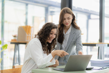 Young attractive caucasian boss and assistant listening financial business consulting with graph paper and tablet laptop on table in officeの写真素材