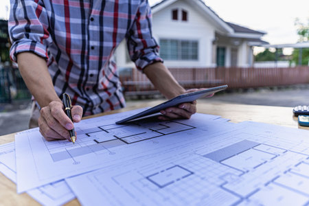 Engineer pointing at blueprint and using laptop to draw building design project in office...