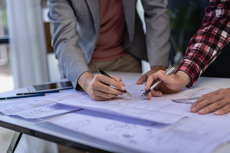 Engineer pointing at blueprint and using laptop to draw building design project in office...