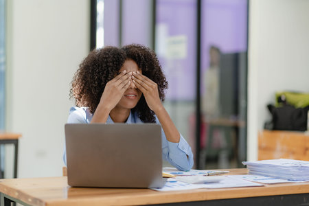 Frustrated business woman with stress headache thinking about a project or deal Massage her head with her hands. She has a headache. She sits at the table. Needs rest.の写真素材
