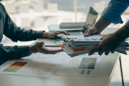 Businessman working in bureaucracy with laptop and documents stacked as graphs in folders and searching for information in office Account budget report file Manage unfinished paperの写真素材