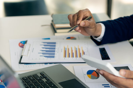 Close up of asian businesswoman hands holding pen and pointing to financial documents and investment plans for business and stocks and graph charts for investment analysis in his oの写真素材