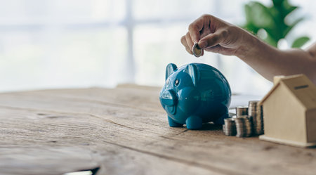 House of piles of coins in front notebook and pen Young man writing by hand. Prepare a plan. Saving coins to buy a house as real estate.の写真素材