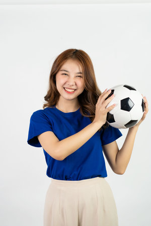Happy Asian female soccer fan in blue shirt cheering for favorite team with soccer ball isolated on white background, pretty young pretty girl holding soccer ball, sports conceptの写真素材