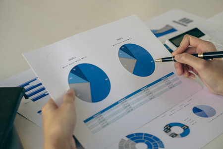 Asian ying businessman hand holding pen pointing at document. Financial graph. Plan. Marketing graph. Finance investment report and business strategy and working on laptop in officの写真素材