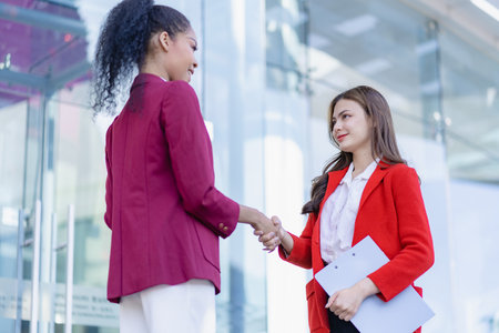Cheerful professional woman holding hands of client or client making business deal in front of office at window Businesswoman greeting colleagues outdoorsの写真素材