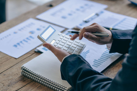 Accountant pressing calculator to make monthly financial report or company profit at desk and calculate income, taxes and expenses. Invoice. Credit card for employee payroll.の写真素材