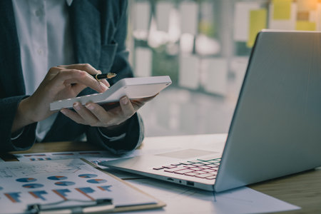 Accountant pressing calculator to make monthly financial report or company profit at desk and calculate income, taxes and expenses. Invoice. Credit card for employee payroll.の写真素材