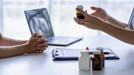 Doctor and patient giving consultation and diagnosis sitting together At table near window in hospital medicine concept with pill bottle and prescription sheet with laptop besideの写真素材