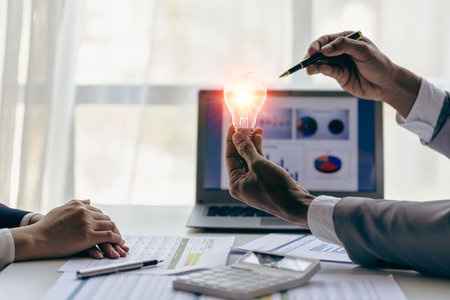 Hand holding a light bulb. Innovation and inspirational concept, businessman holding light bulb hand with financial documents and new concept tools for business and finance.の写真素材