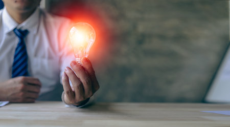 Hand holding a light bulb. Innovation and inspirational concept, businessman holding light bulb hand with financial documents and new concept tools for business and finance.の写真素材