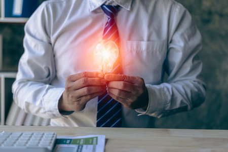 Hand holding a light bulb. Innovation and inspirational concept, businessman holding light bulb hand with financial documents and new concept tools for business and finance.の写真素材