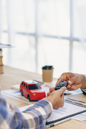 Explain promotions and car insurance for rental or purchase. A car dealer or sales manager hands the keys to the car owner and explains the terms of the car contract at a desk in tの写真素材