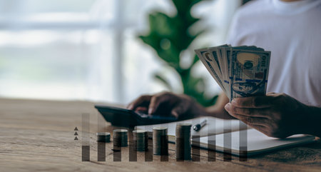 Young man is using pen to record amount of money and coins for accounting plan on wooden table in home office, accounting and finance calculation conceptの写真素材