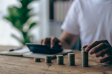 Young man is using pen to record amount of money and coins for accounting plan on wooden table in home office, accounting and finance calculation conceptの写真素材