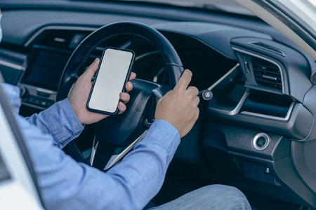 Man holding a smartphone with a blank screen Mobile phone against the background of a car steering wheel A phone with a blank screen for inscriptions or pictures. transport and vehの写真素材