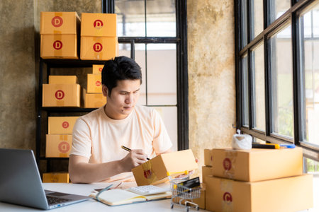 Asian Male SME Small Business Entrepreneur, freelance working from home using laptop for commercial auditing. online marketing Packaging Box SME Seller Concept Ecommerce Team onlinの写真素材