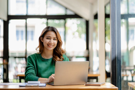young woman working in a cafe using laptop and drinking coffee Asian female student using a computer for distance learning sitting on a bench in the shop casual lifestyle people anの写真素材