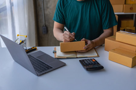 Small business owner starting a SME. Asian man checking online orders, selling products, working with boxes. home office freelance work online work sme business delivery conceptの写真素材