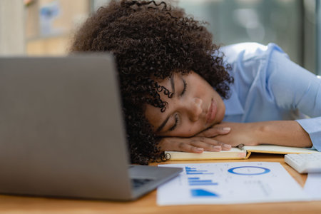 Tired young african american woman sleeping at desk in front of laptop. concept of workの写真素材