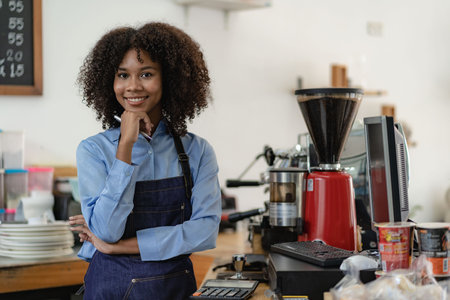 Barista, coffee shop startup, African American female entrepreneur standing in front of the counter. A young female waitress in an apron serving customers in a storeの写真素材