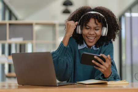 Female student in headphones holding smartphone, playing games and using mobile apps, online distance learning, watching video courses or zoom calls, making notes in workbook sittiの写真素材