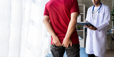 Young man with hemorrhoids consulting a doctor Man touching her buttocks because of abdominal pain and hemorrhoids Health care concept. Man suffering from hemorrhoids and constipatの写真素材