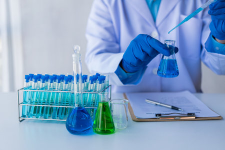 Medical or scientific researcher or male doctor looking at test tube of transparent solution in...