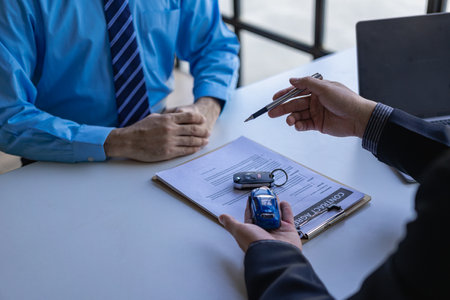 Salesman guiding customer seated at table. Car business. Car sale. Dealership closing. and the new owner has entered into a contract The idea of ââselling and renting a car with inの写真素材