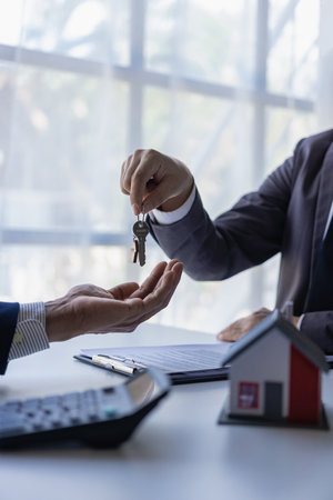 real estate agent insurance sales representative And a young Asian businessman handing over the keys to the home buyer and a model house after signing the sale contract at the tablの写真素材