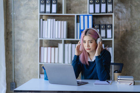 Asian female college student wearing headphones studying online with laptop computer surfing...