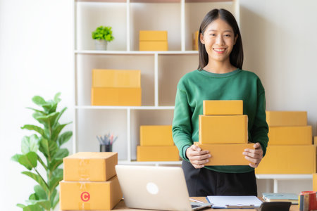 An excited Asian female small business owner works in her room while using her laptop computer to...