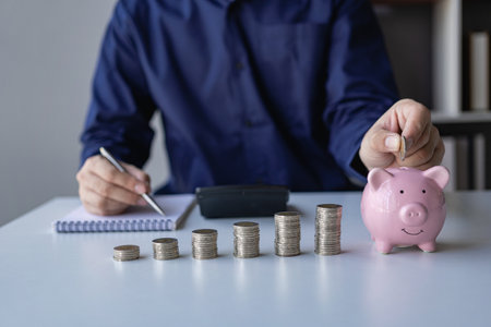 Businessman calculating savings with pile of coins on table, importance of bank and piggy bank to business, investment and financial stabilityの写真素材